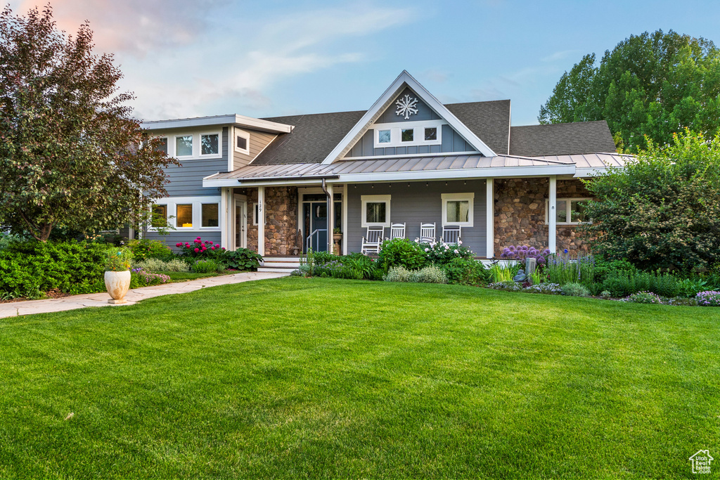 View of front of home featuring stone siding, a standing seam roof, a front yard, and a metal roof