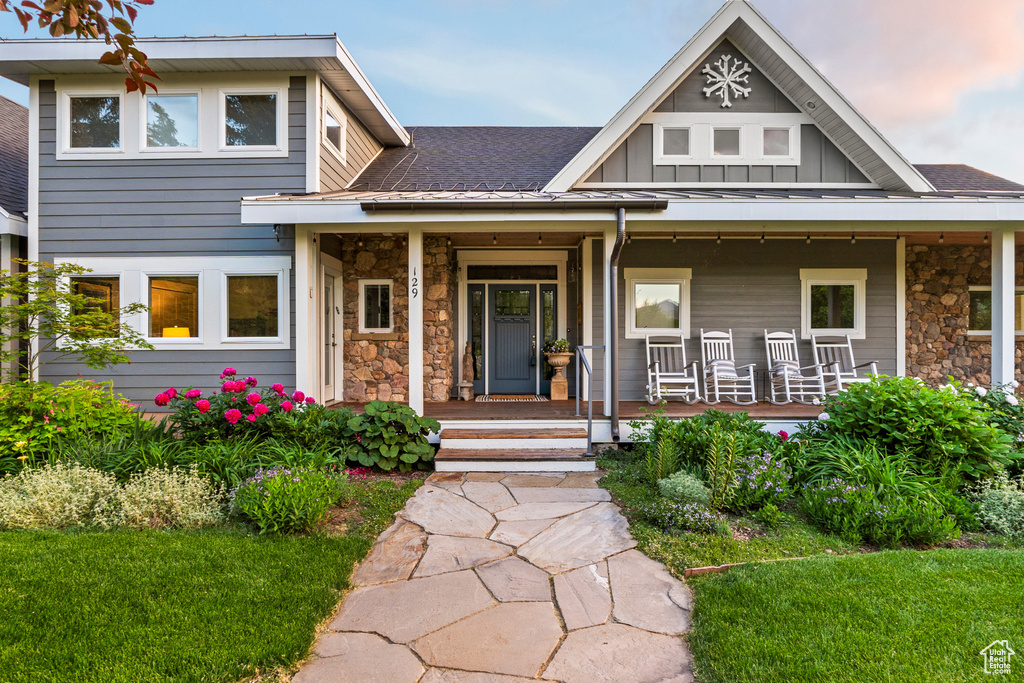 View of front facade featuring stone siding, covered porch, a shingled roof, and board and batten siding