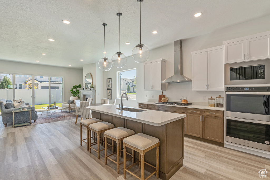Kitchen with light countertops, appliances with stainless steel finishes, a sink, open floor plan, and wall chimney range hood