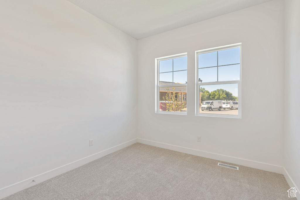 Unfurnished room featuring baseboards, visible vents, and light colored carpet