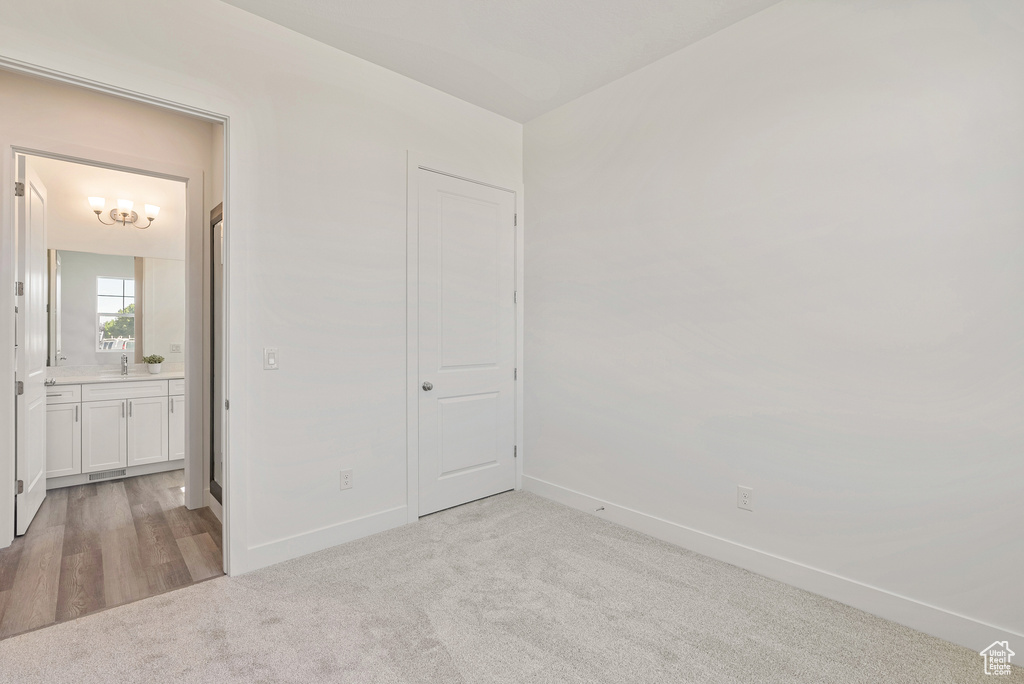 Unfurnished bedroom featuring a sink, light carpet, baseboards, and ensuite bathroom