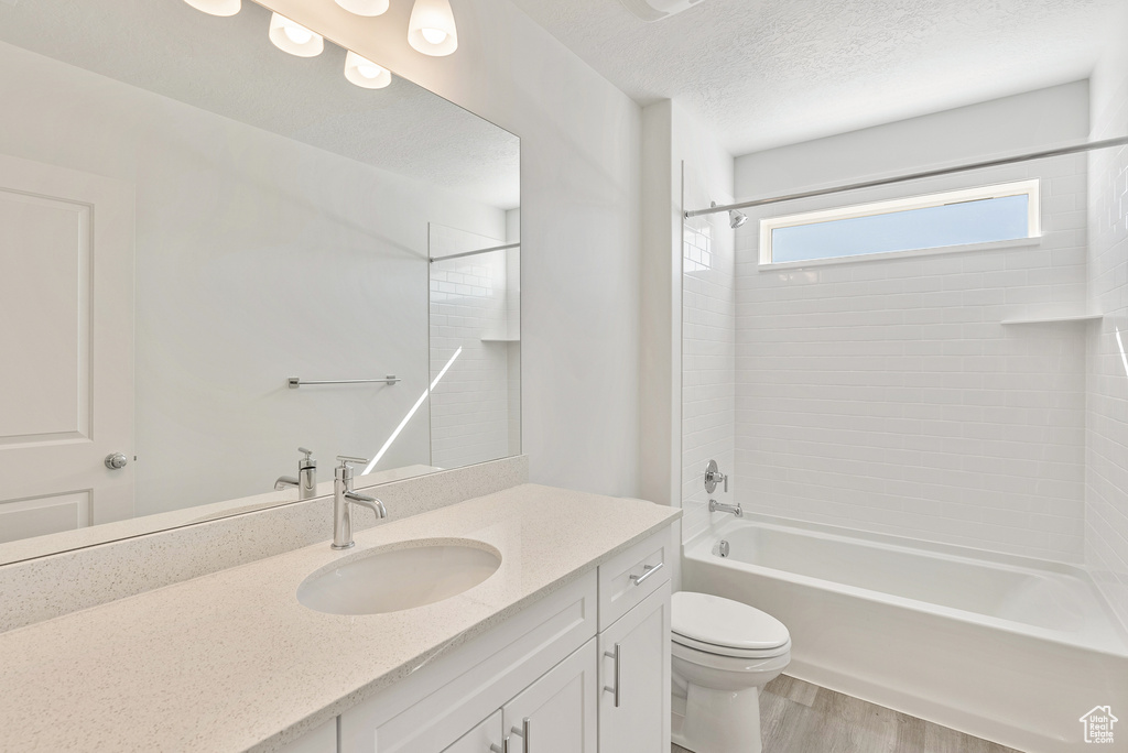 Full bath with toilet, vanity, wood finished floors, a textured ceiling, and tub / shower combination