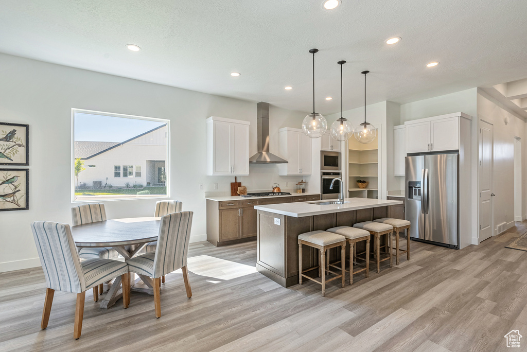 Kitchen featuring wall chimney exhaust hood, appliances with stainless steel finishes, an island with sink, a sink, and a breakfast bar area