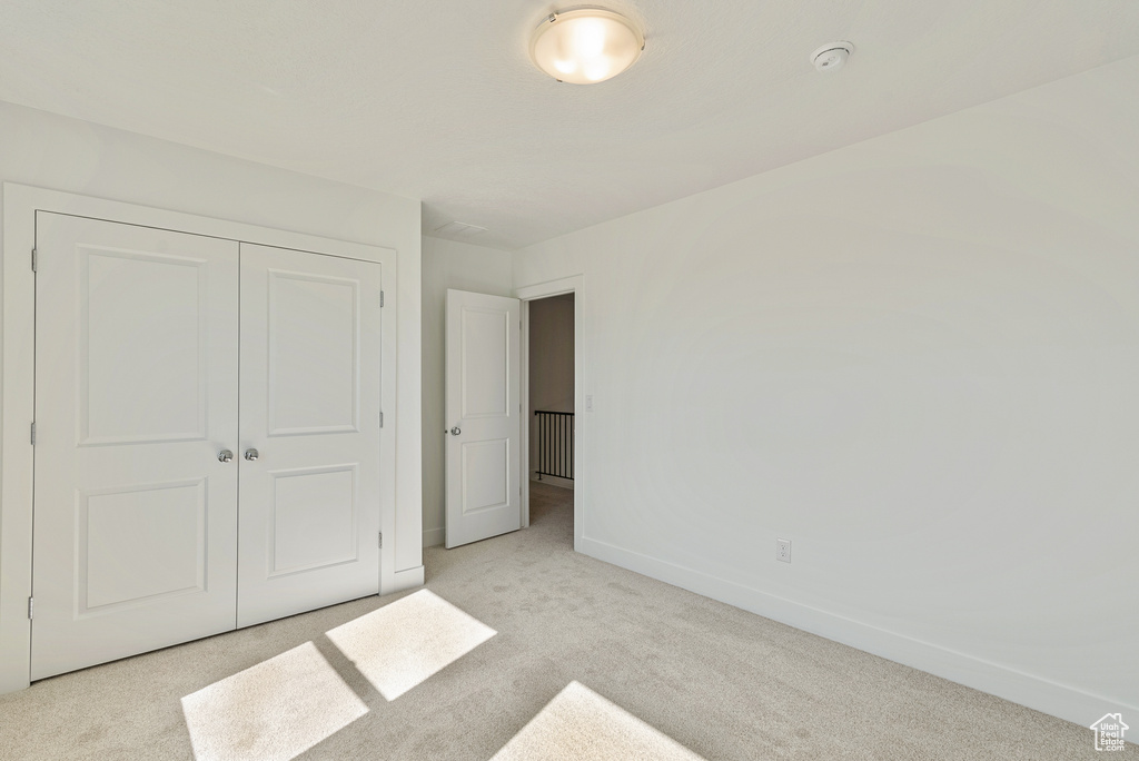 Unfurnished bedroom featuring a closet, baseboards, and light carpet