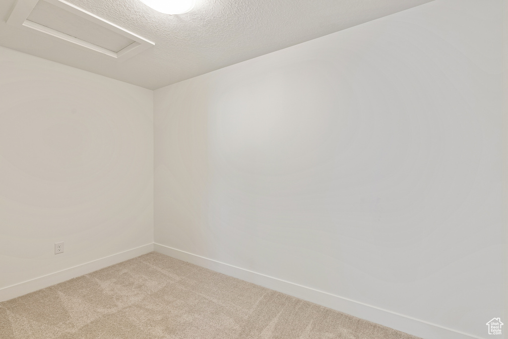 Unfurnished room featuring light carpet, baseboards, attic access, and a textured ceiling