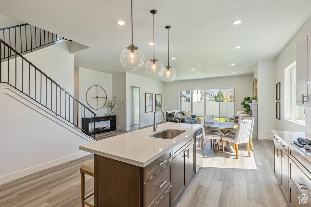 Kitchen featuring light wood-style flooring, dishwasher, baseboards, a sink, and open floor plan