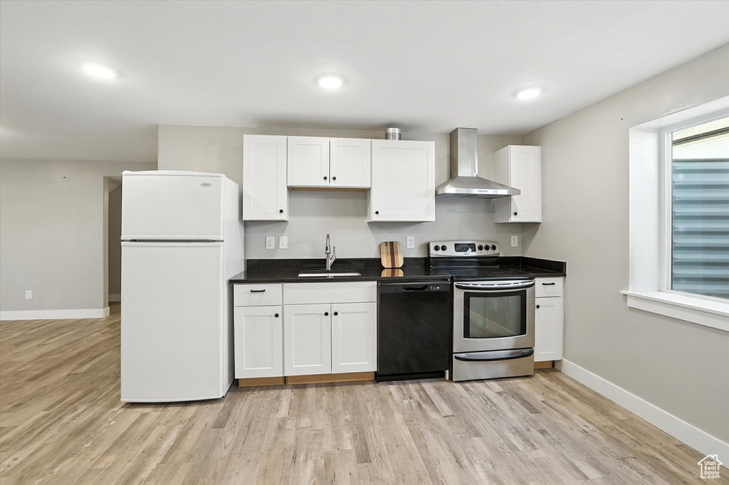 Kitchen featuring freestanding refrigerator, black dishwasher, wall chimney exhaust hood, electric stove, and light wood-style floors
