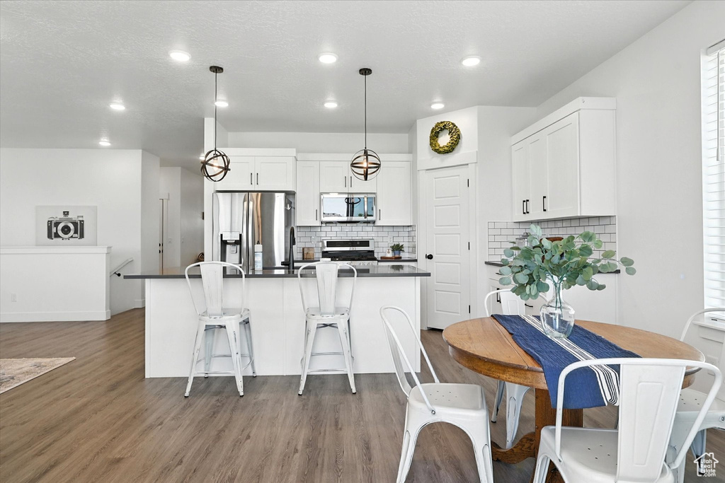Kitchen with stove, stainless steel fridge, dark countertops, wood finished floors, and backsplash