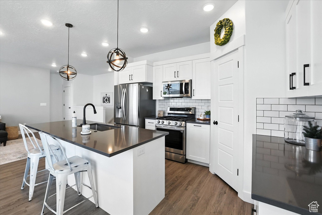 Kitchen with stainless steel appliances, dark countertops, dark wood-style floors, a kitchen breakfast bar, and recessed lighting