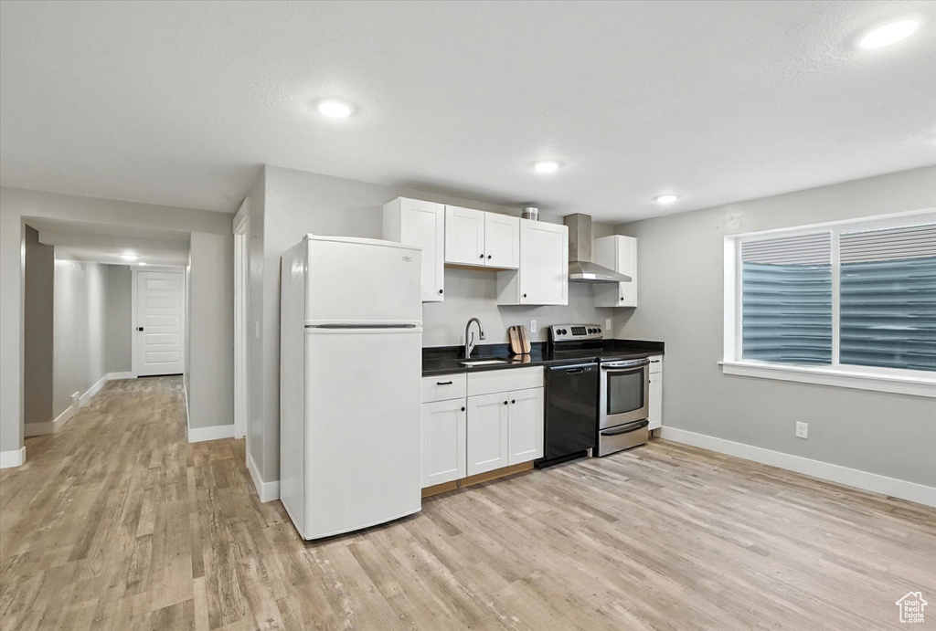 Kitchen featuring freestanding refrigerator, electric range, wall chimney range hood, dishwashing machine, and light wood-type flooring