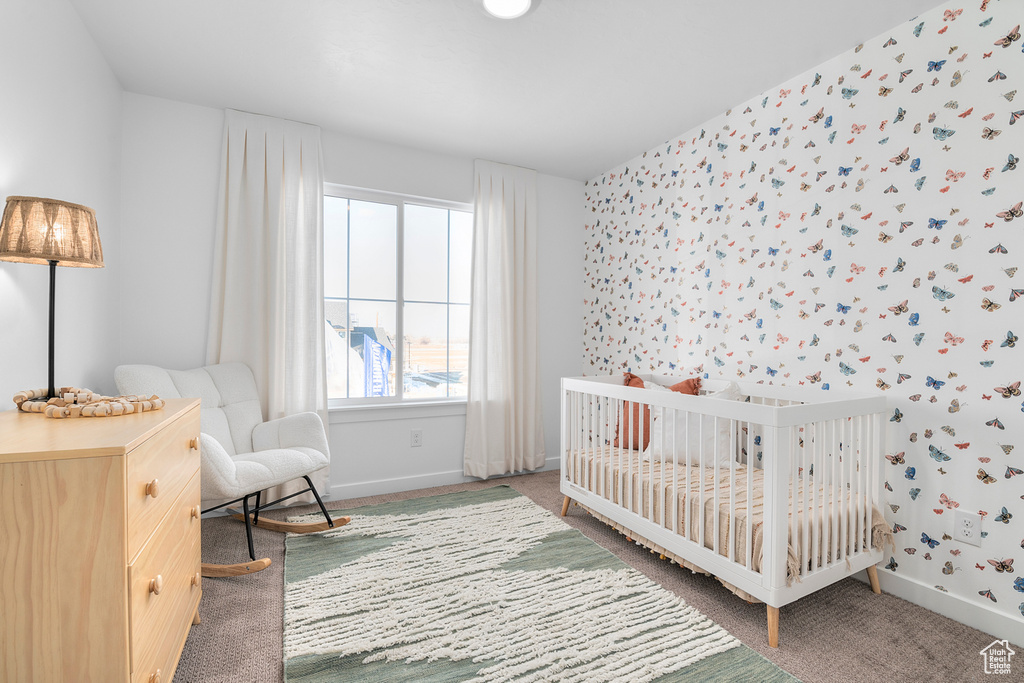 Bedroom with carpet flooring, wallpapered walls, a crib, and baseboards