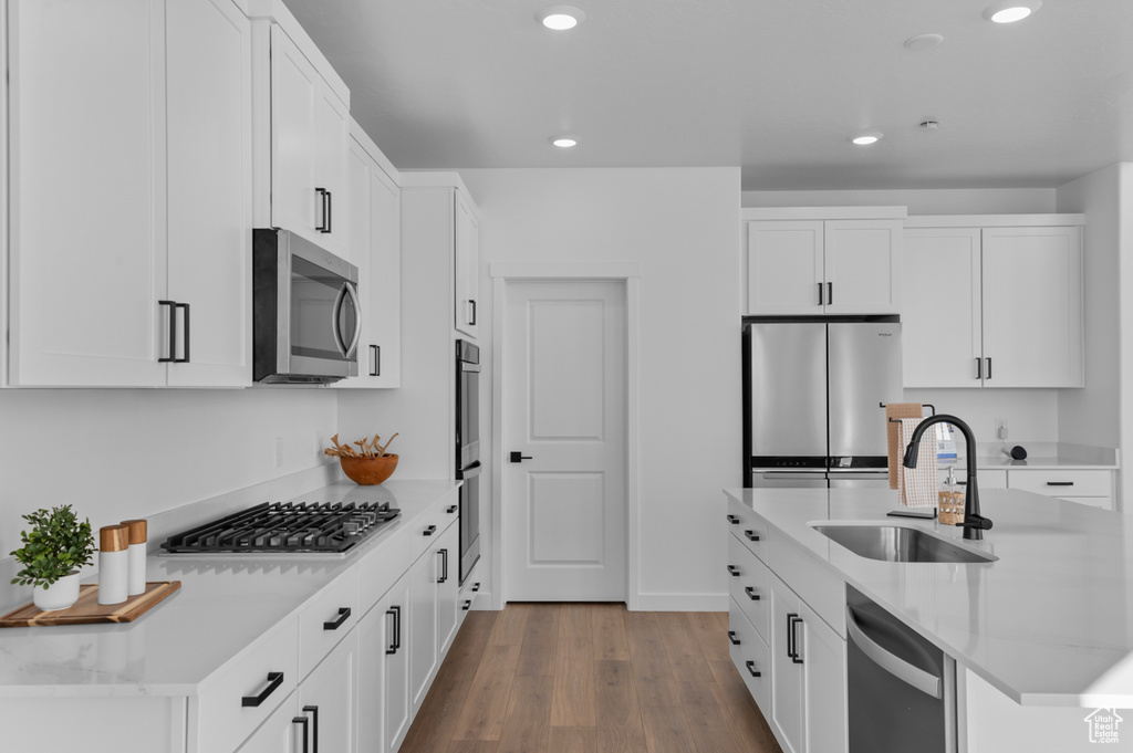 Kitchen featuring white cabinetry, wood finished floors, a sink, and stainless steel appliances