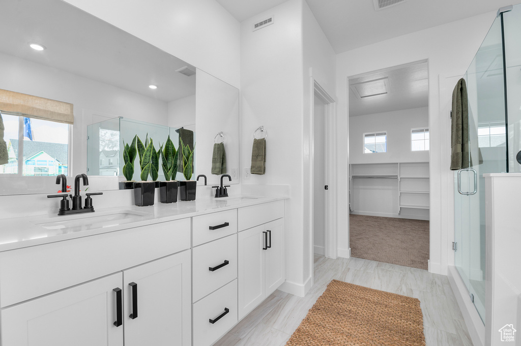 Full bath with a spacious closet, double vanity, a sink, and a stall shower