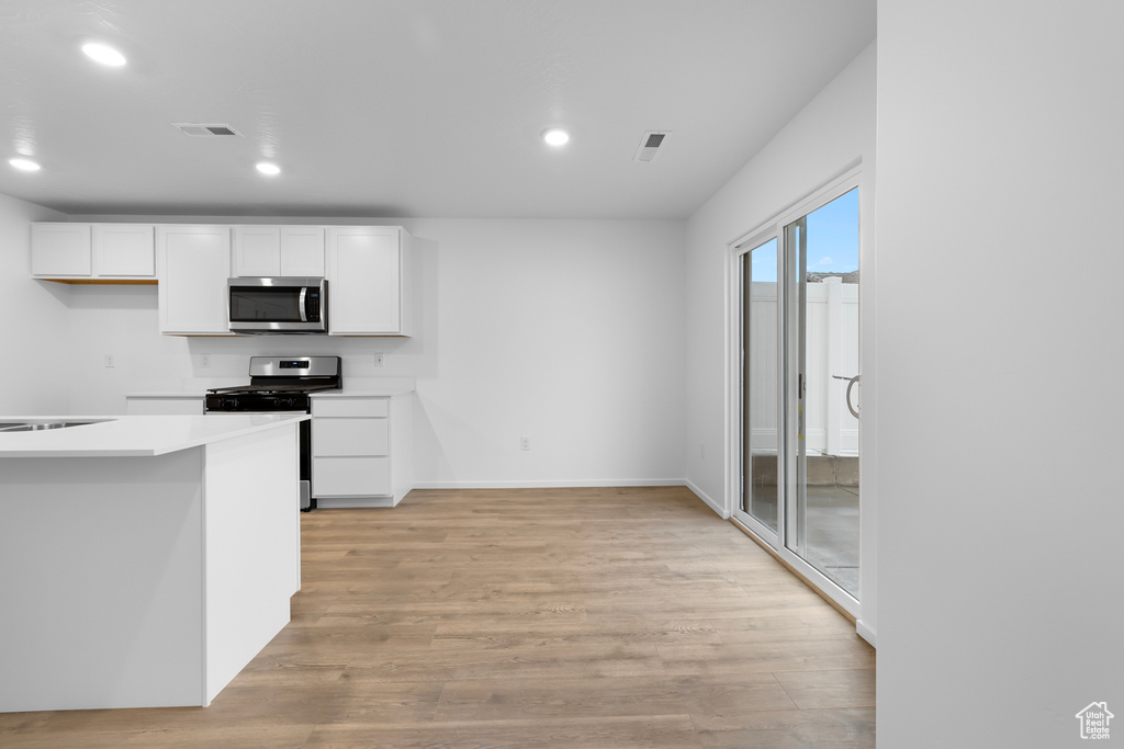 Kitchen featuring light countertops, light wood-style flooring, stainless steel appliances, recessed lighting, and white cabinetry