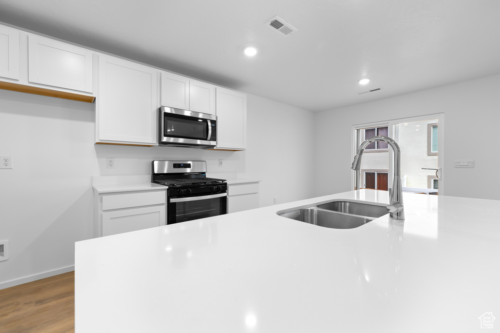 Kitchen featuring light countertops, a sink, light wood-style flooring, stainless steel appliances, and white cabinets