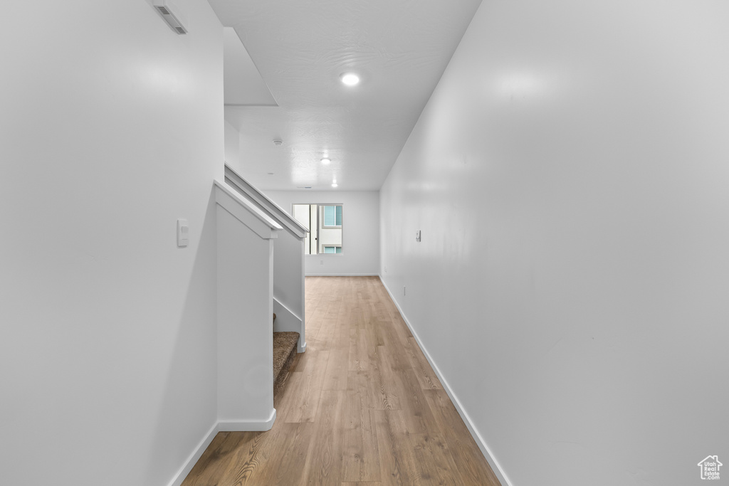 Hall with light wood finished floors, baseboards, visible vents, and stairway