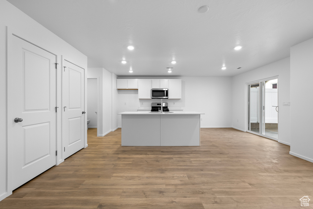 Kitchen featuring white cabinetry, stainless steel appliances, light wood-type flooring, and a center island with sink