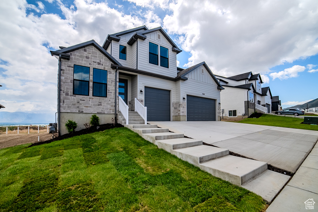 View of front of house with board and batten siding, driveway, stone siding, a front yard, and an attached garage