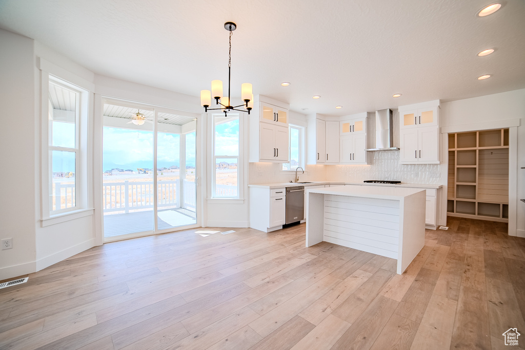 Kitchen featuring an inviting chandelier, dishwasher, wall chimney range hood, light countertops, and backsplash