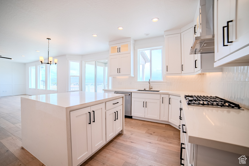 Kitchen with appliances with stainless steel finishes, a center island, light wood-type flooring, a sink, and wall chimney exhaust hood