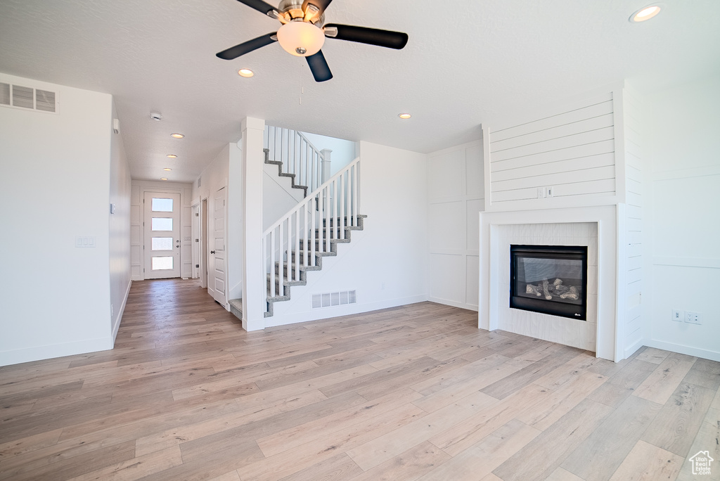 Unfurnished living room featuring a glass covered fireplace, stairway, light wood-style flooring, and visible vents