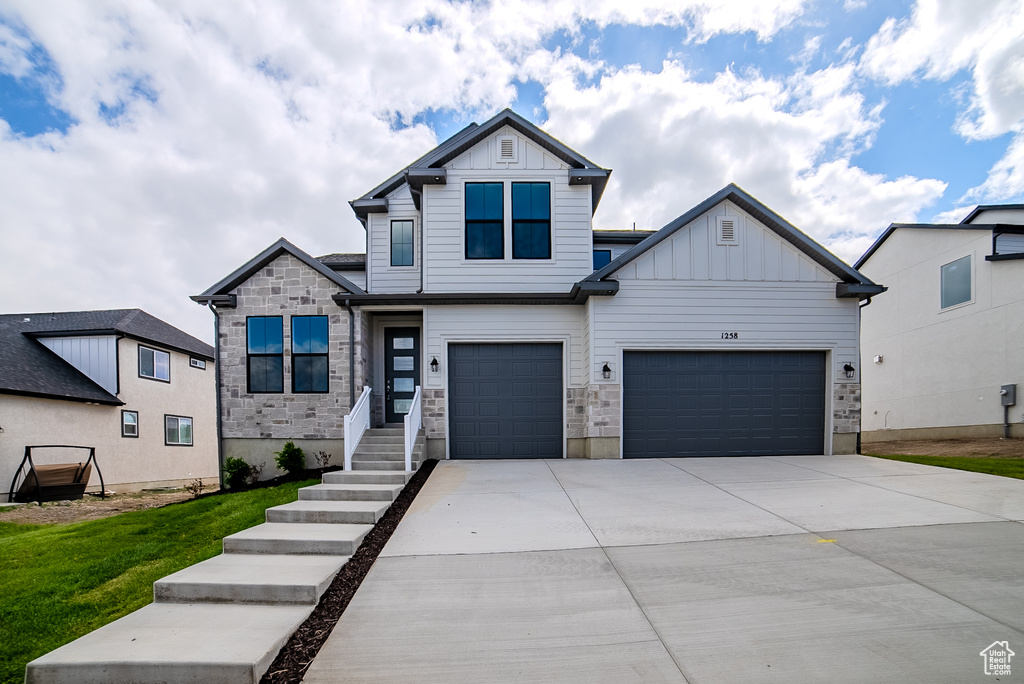 View of front of house featuring board and batten siding, concrete driveway, stone siding, a front yard, and an attached garage