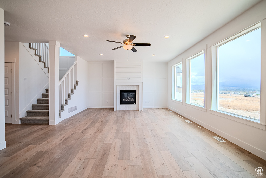 Unfurnished living room featuring visible vents, stairs, ceiling fan, and light wood-style floors