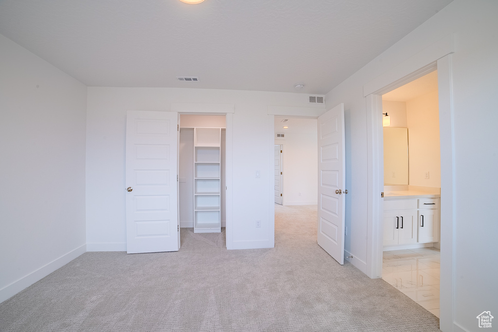 Unfurnished bedroom featuring visible vents, baseboards, a walk in closet, and light colored carpet