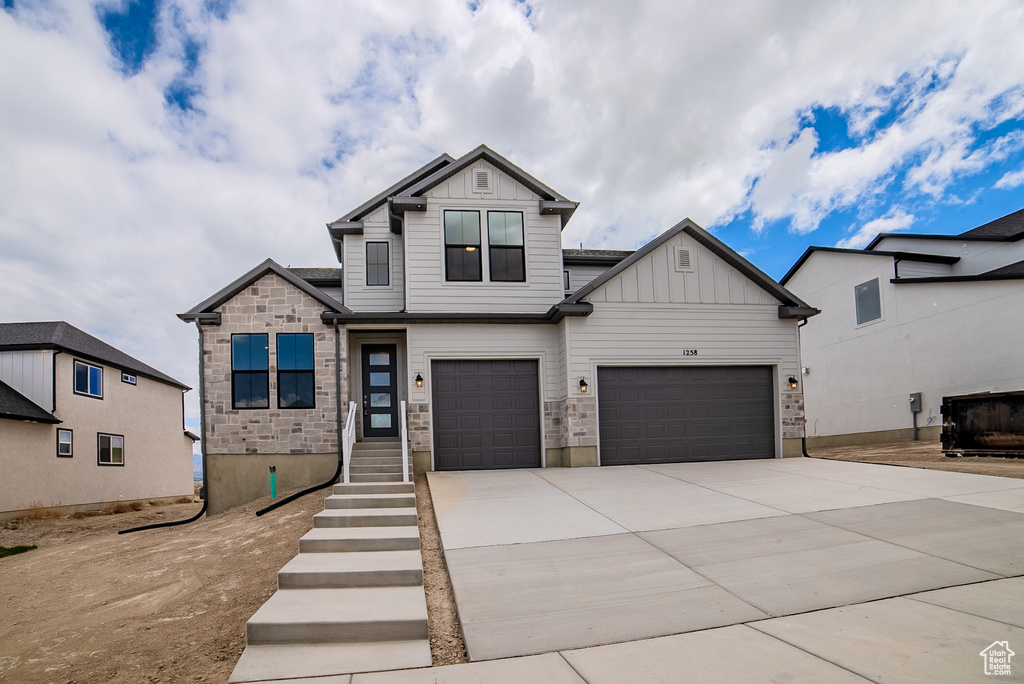 Craftsman-style home featuring board and batten siding, an attached garage, driveway, and stone siding