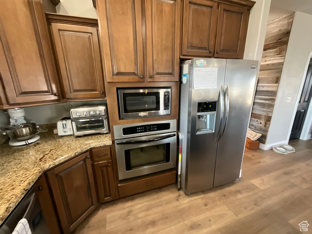 Kitchen with stainless steel appliances, light stone countertops, light wood-style floors, and baseboards
