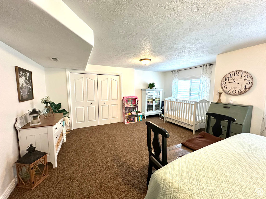 Bedroom with a textured ceiling, dark carpet, a closet, and baseboards