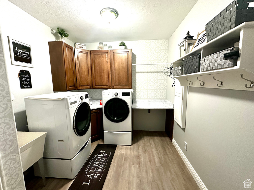 Laundry area featuring cabinet space, light wood-style flooring, washing machine and dryer, and a textured ceiling