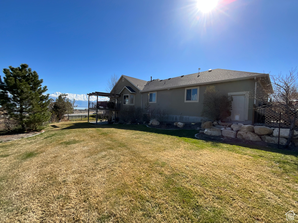 Rear view of property featuring roof with shingles, stucco siding, and a yard