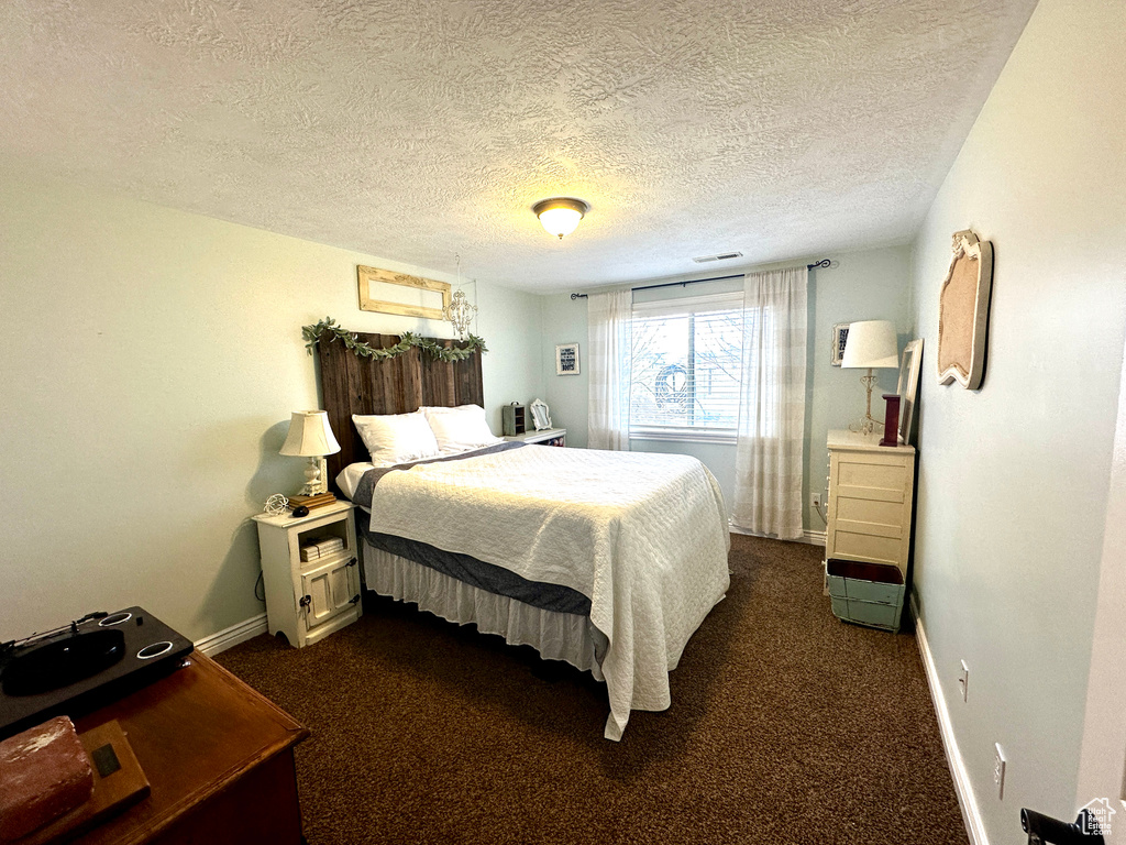 Bedroom featuring visible vents, baseboards, dark carpet, and a textured ceiling
