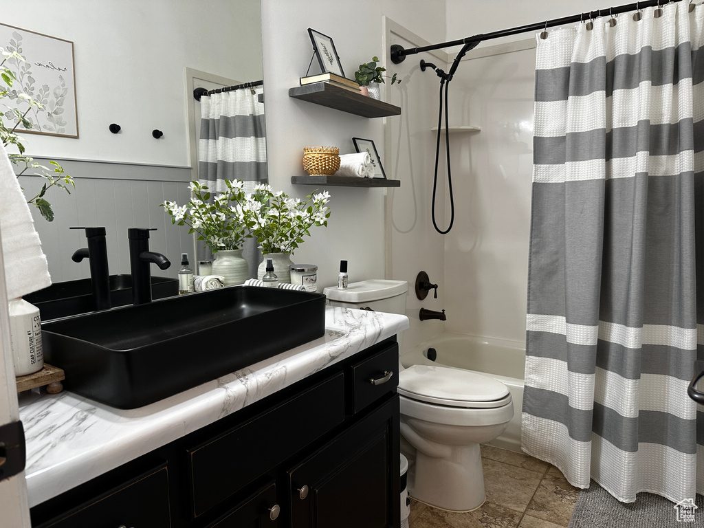 Full bath with toilet, vanity, wainscoting, and shower / bath combination with curtain
