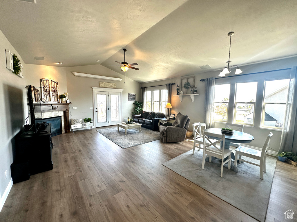 Dining space featuring a glass covered fireplace, ceiling fan with notable chandelier, vaulted ceiling, and wood finished floors