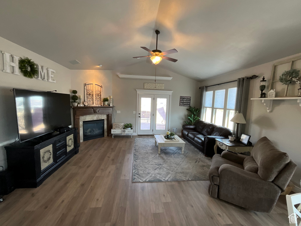Living room with ceiling fan, a glass covered fireplace, vaulted ceiling, and wood finished floors