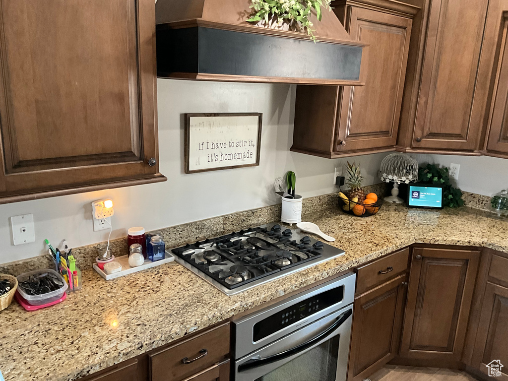 Kitchen with light stone countertops, dark brown cabinetry, wall chimney exhaust hood, and appliances with stainless steel finishes