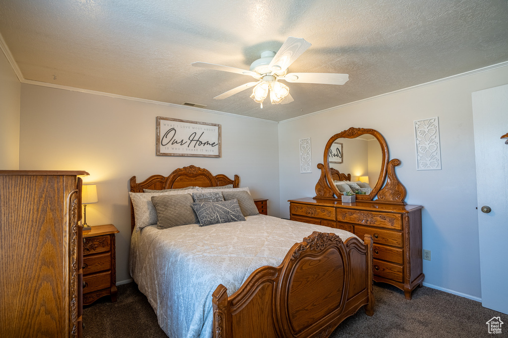 Bedroom featuring dark carpet, a textured ceiling, visible vents, and ornamental molding