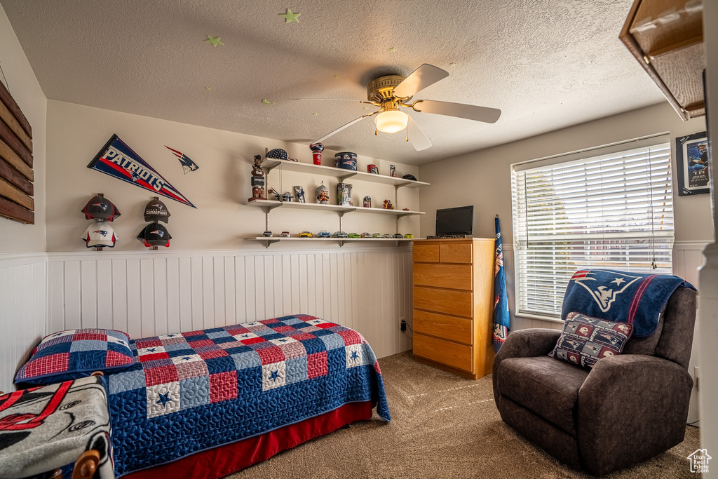 Bedroom featuring a wainscoted wall, carpet floors, ceiling fan, and a textured ceiling