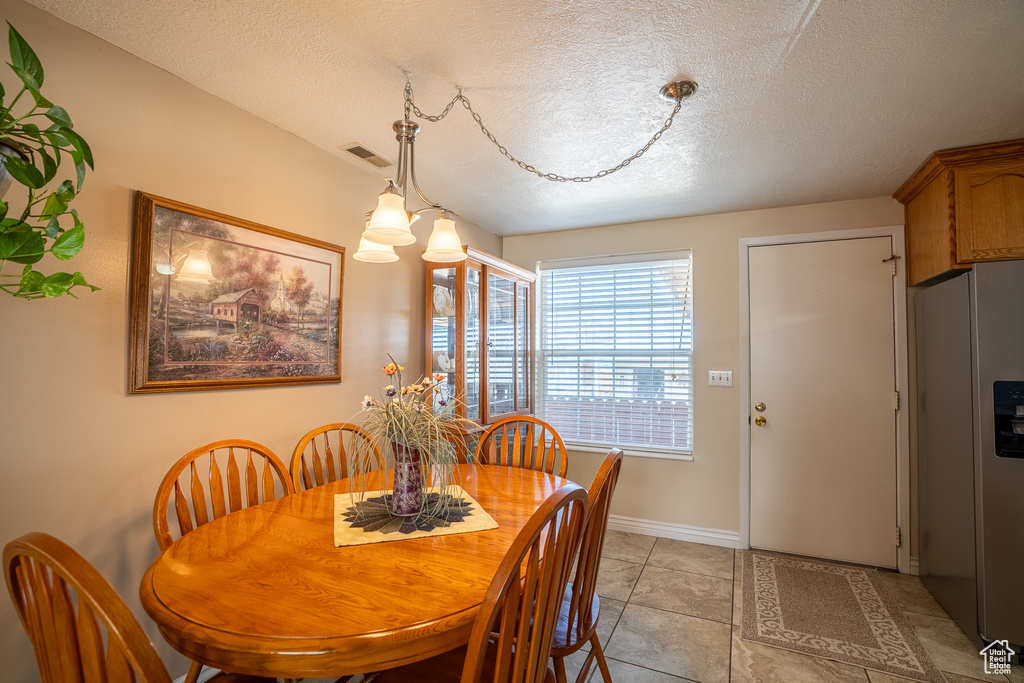 Dining area featuring light tile patterned floors, a textured ceiling, baseboards, and visible vents