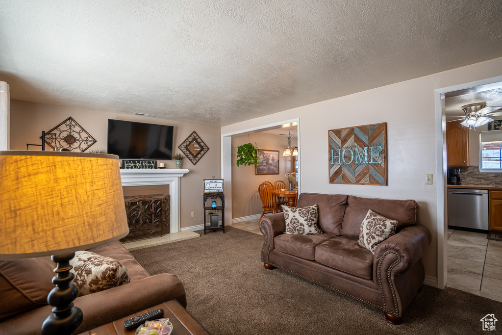 Carpeted living room with a ceiling fan, a fireplace with raised hearth, baseboards, and a textured ceiling