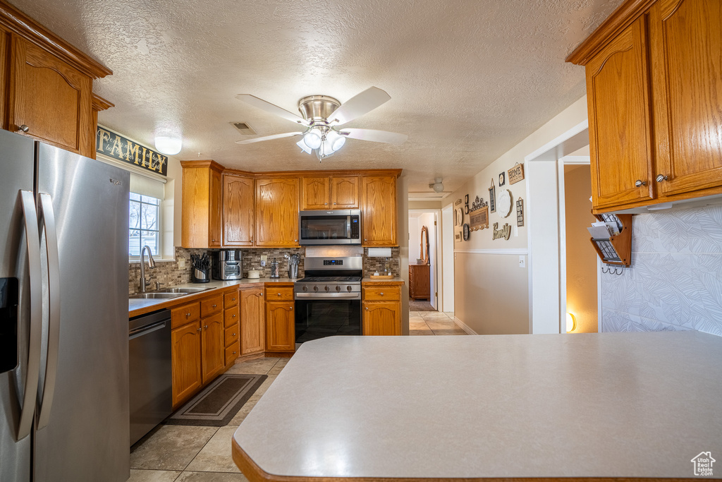 Kitchen featuring decorative backsplash, brown cabinets, stainless steel appliances, a ceiling fan, and a sink