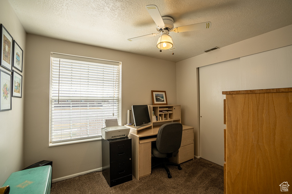 Carpeted office with a textured ceiling, visible vents, baseboards, and a ceiling fan