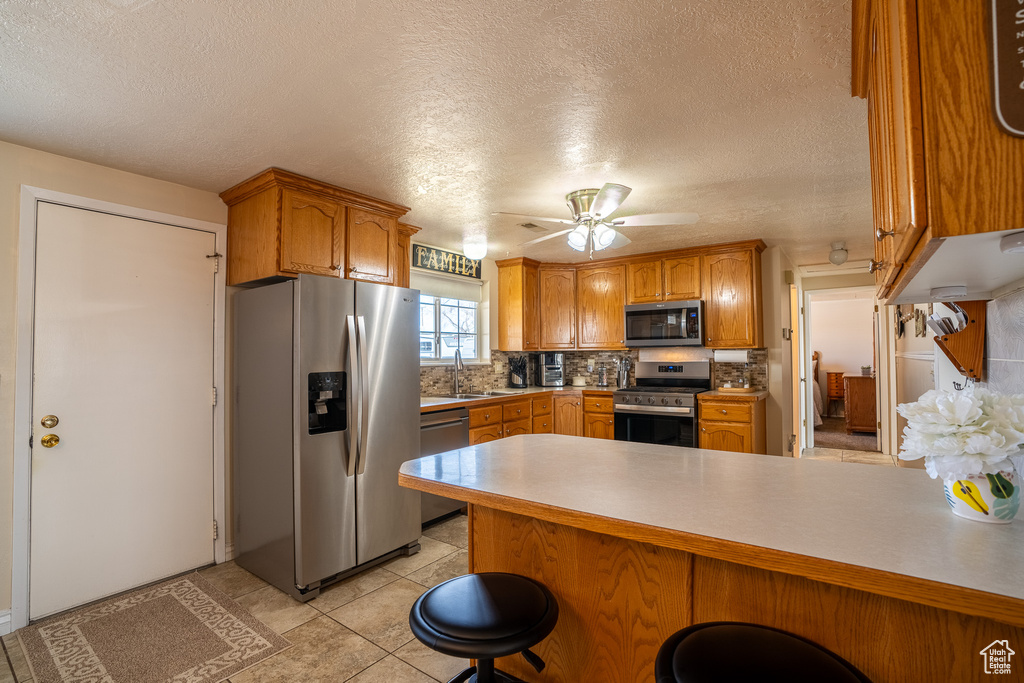 Kitchen with decorative backsplash, a sink, a peninsula, appliances with stainless steel finishes, and brown cabinetry