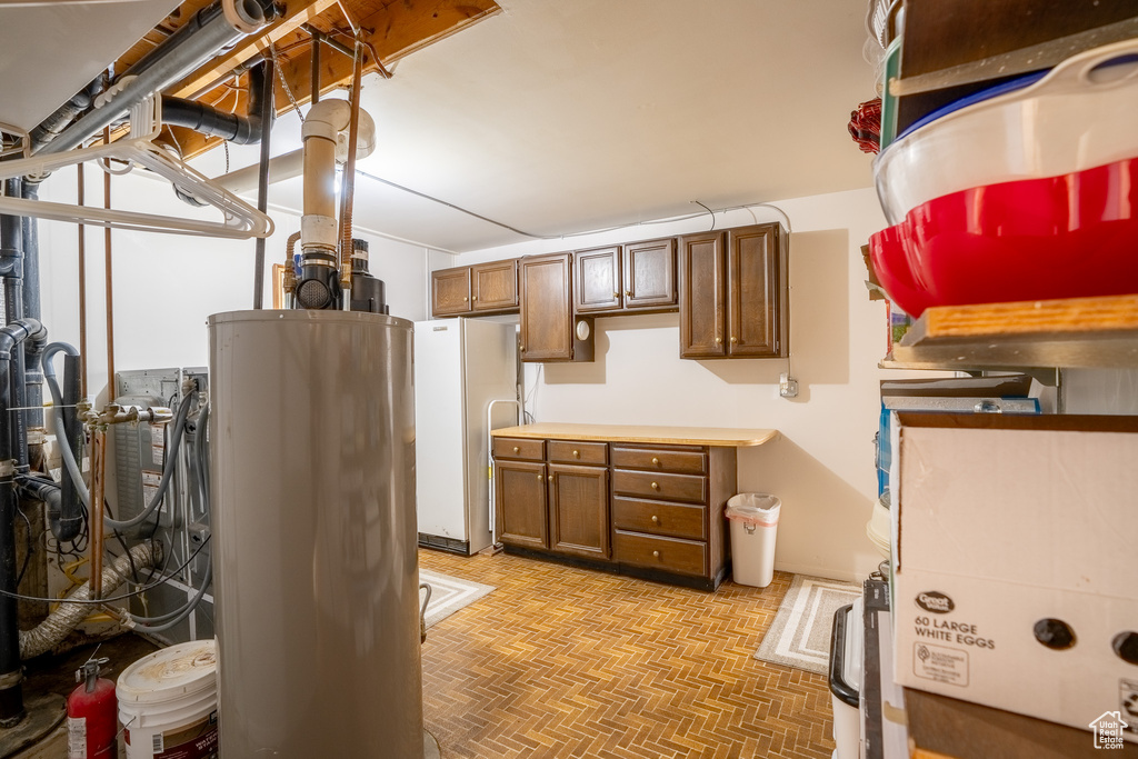 Basement featuring water heater, brick floor, and freestanding refrigerator