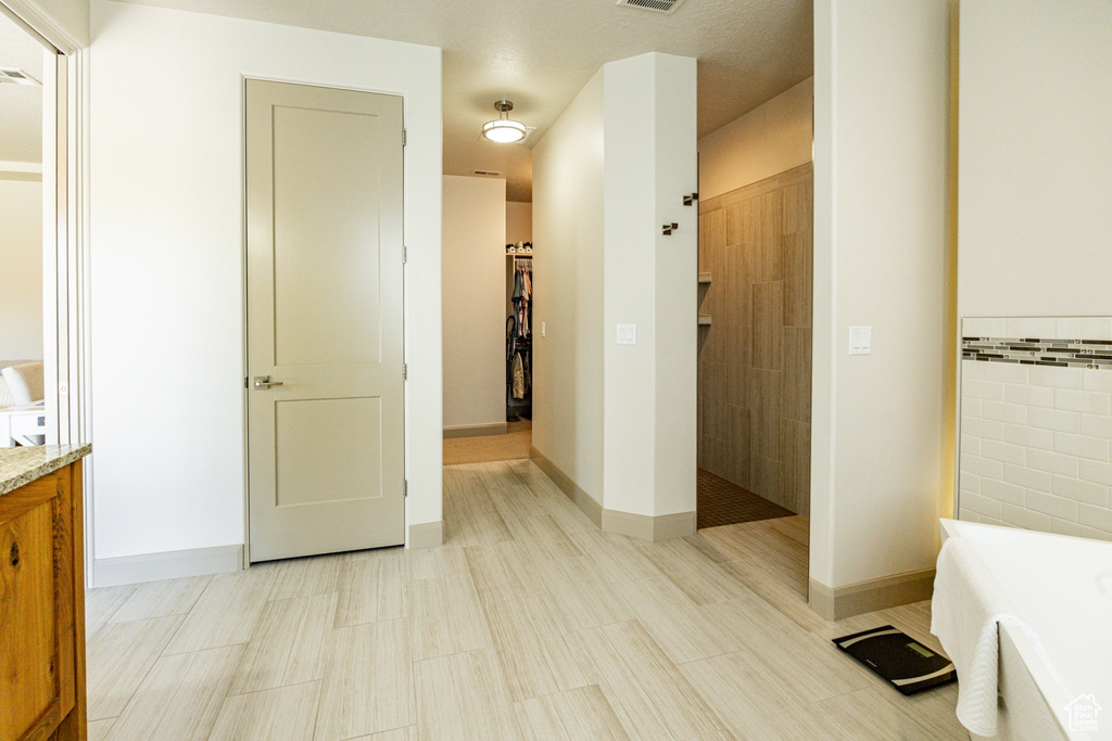 Full bath with a walk in shower, vanity, a walk in closet, visible vents, and a freestanding bath