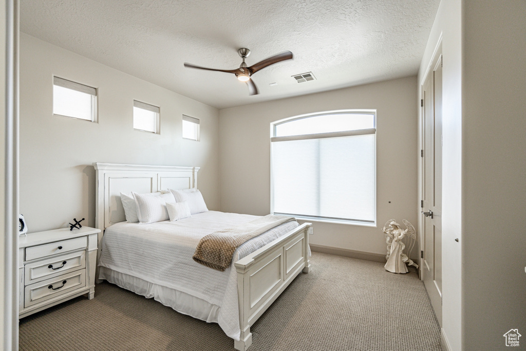 Bedroom with carpet, baseboards, a textured ceiling, visible vents, and a ceiling fan