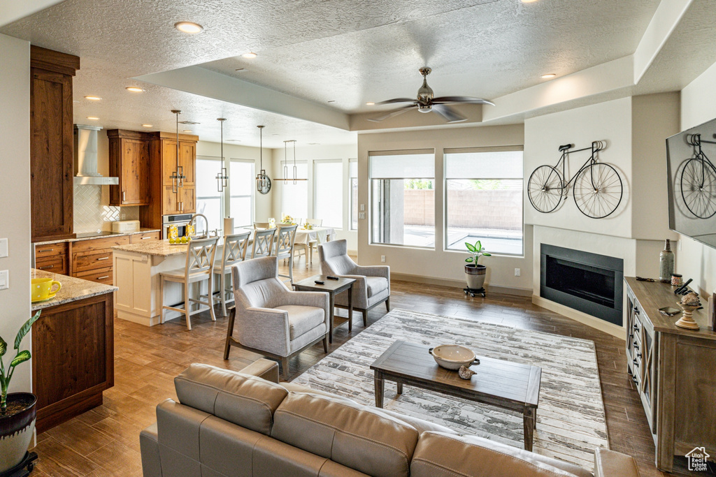 Living room featuring a textured ceiling, baseboards, a fireplace, ceiling fan, and wood finished floors