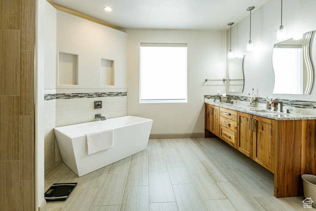 Bathroom featuring tile walls, baseboards, a soaking tub, a sink, and double vanity